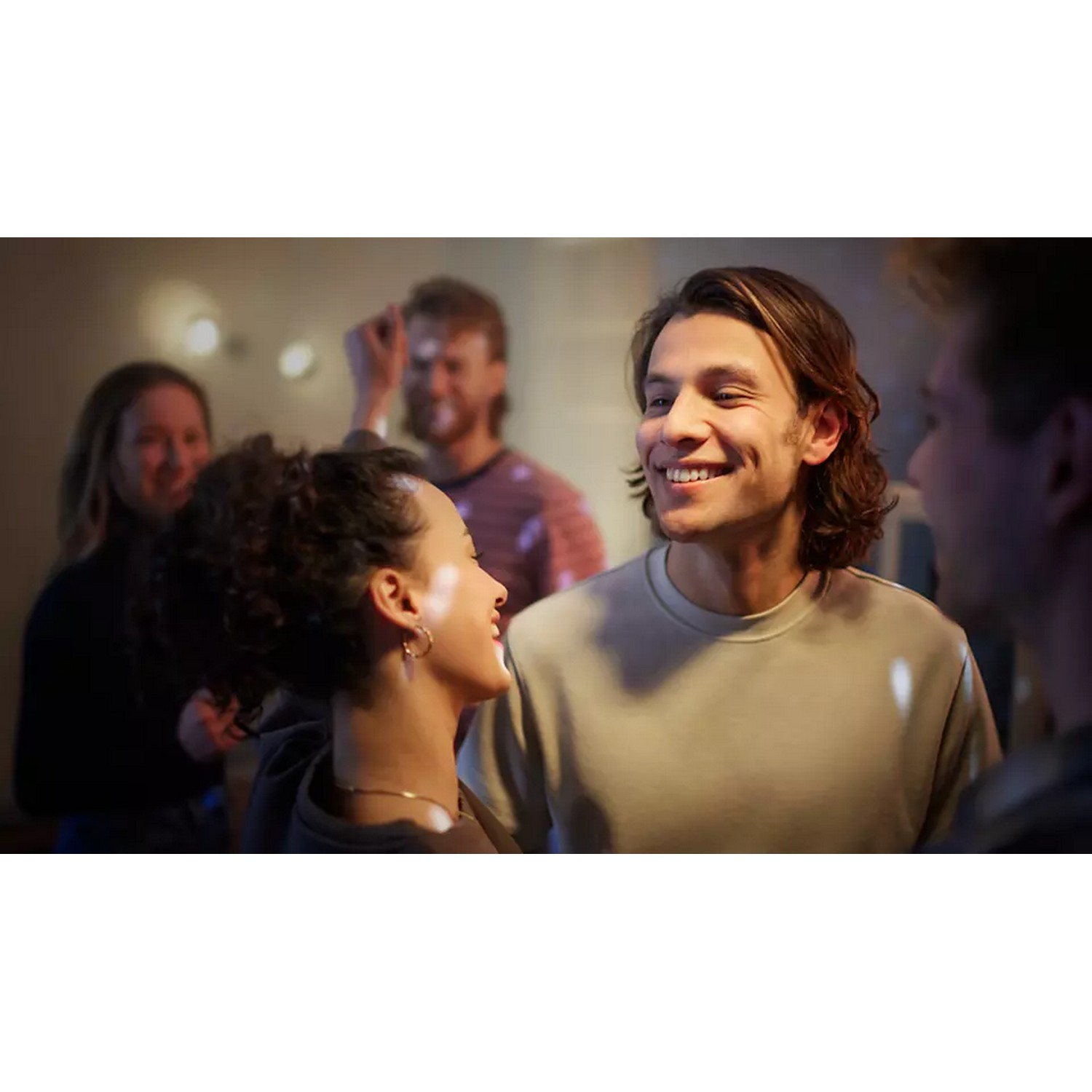 A man and woman smiling at each other in a brightly lit room with other people.