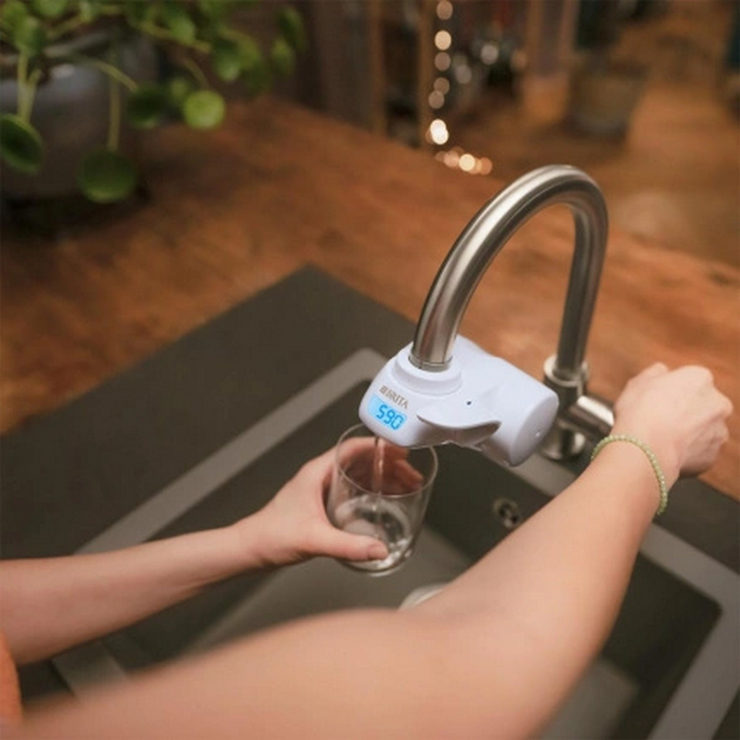 Een persoon die een glas vult met water uit een kraan met een digitaal display.