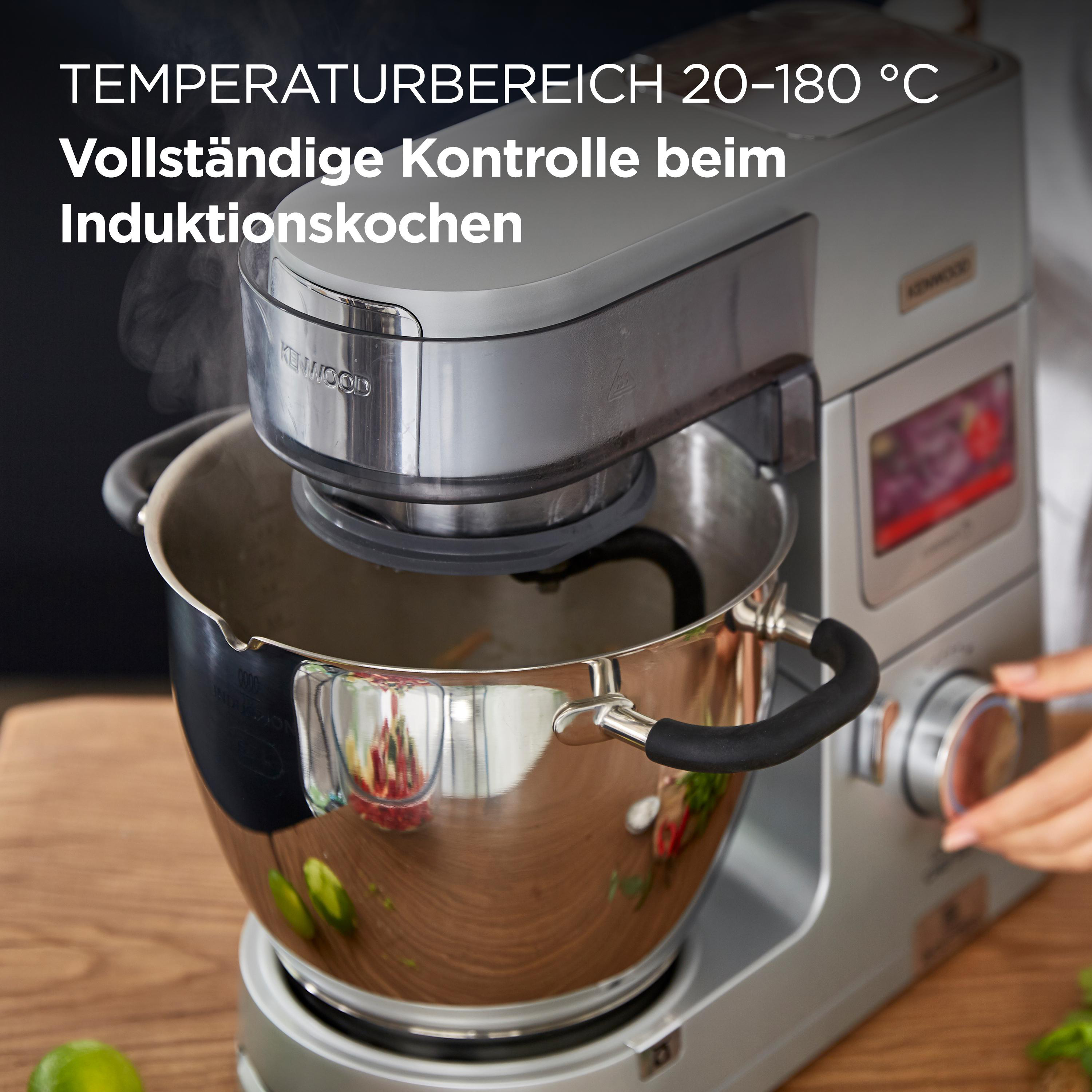 Ein silberner Küchenmixer mit Dampf, der aus einer Edelstahlschüssel aufsteigt, eine Hand ist sichtbar.