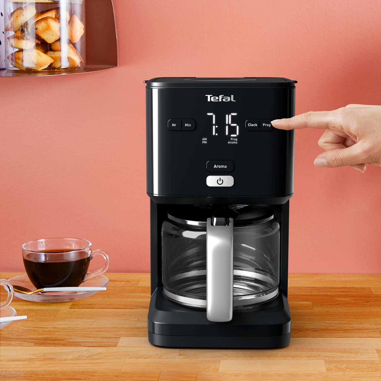 Zwart koffiezetapparaat met een digitale display die 7:15 laat zien. Een hand drukt op een Prog knop.