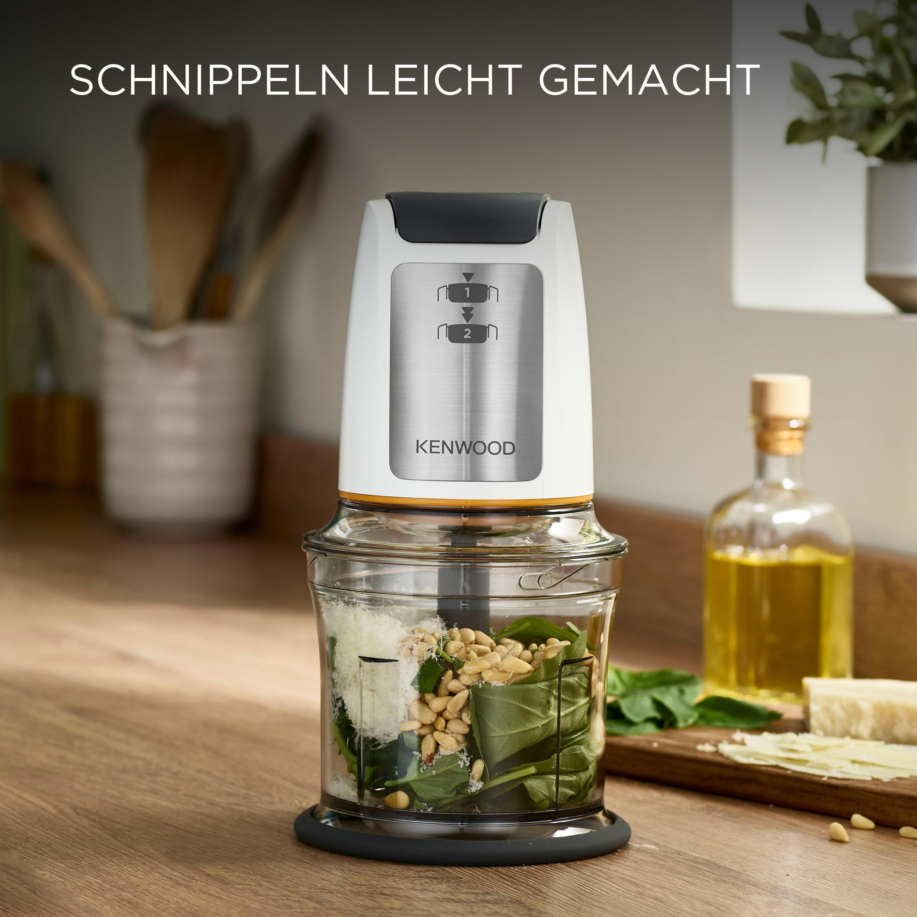 Ein Kenwood-Zerkleinerer mit Zutaten im Inneren. Artikel stehen auf einer Holztheke.