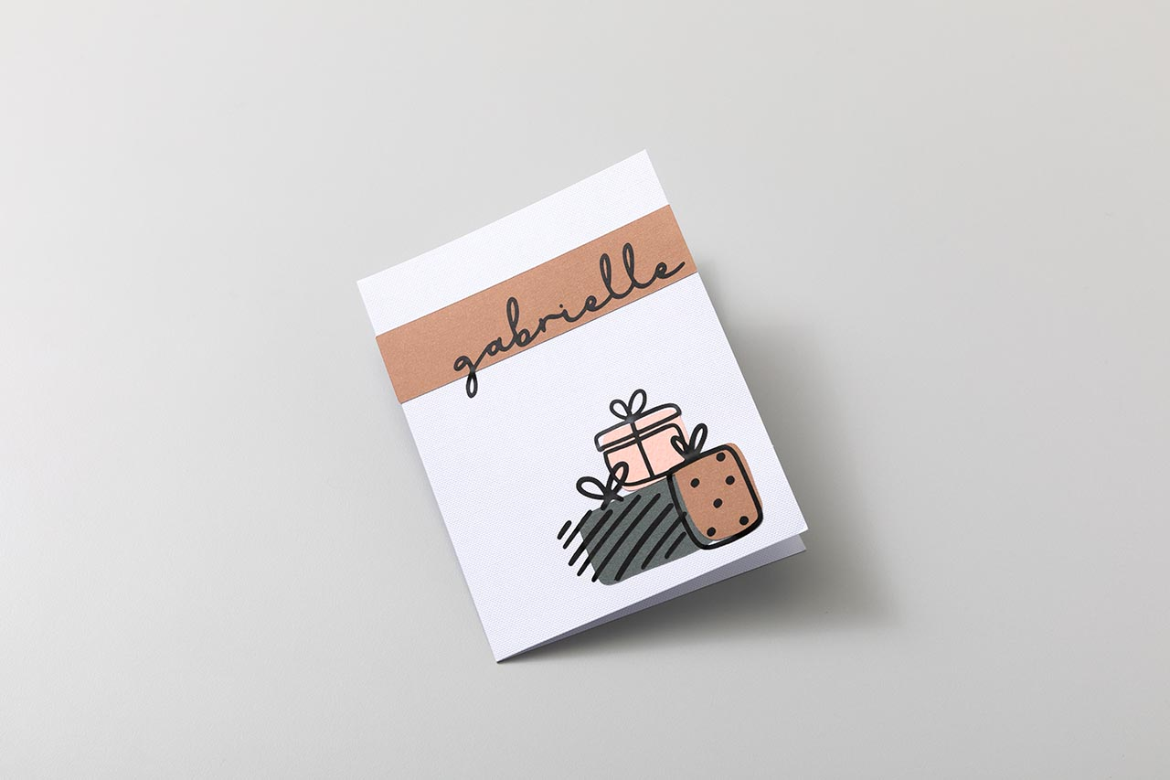 Weiße Karte mit 'gabrielle' in Schrift, braunem Band und Geschenk-Icons.