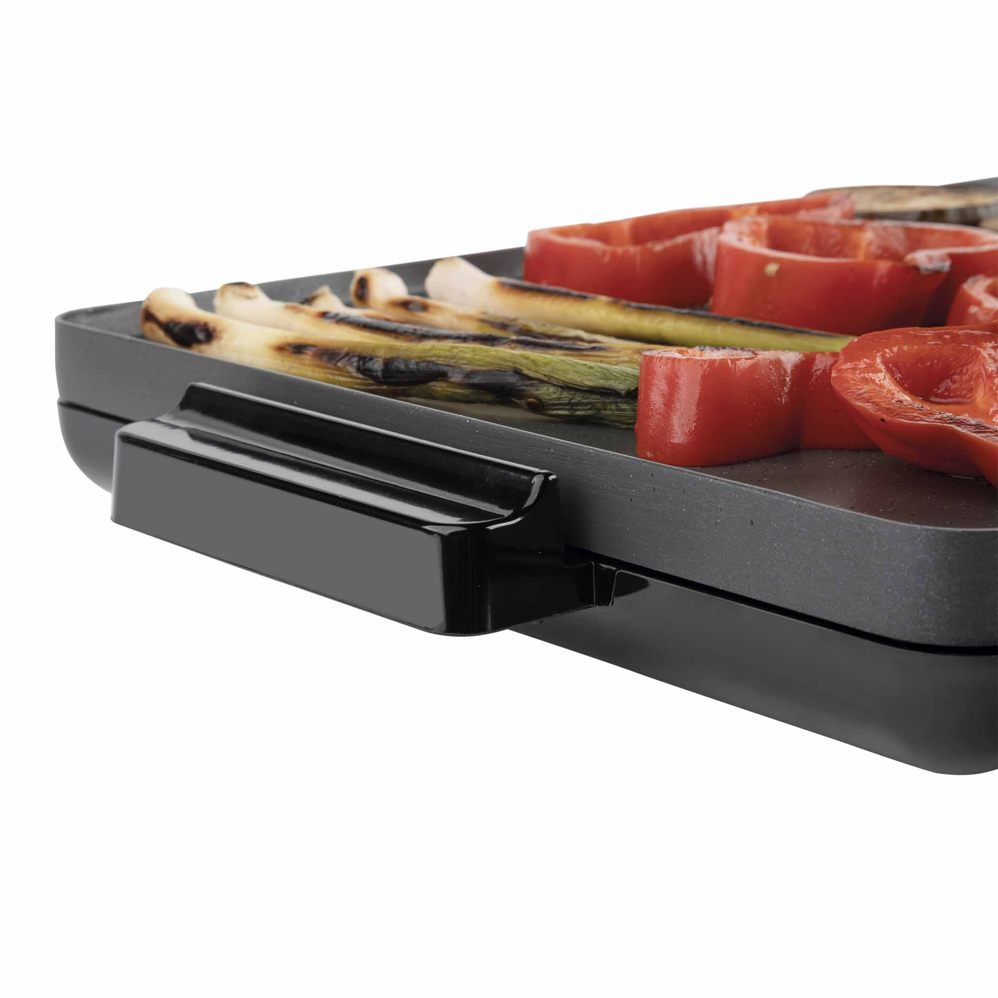 Primer plano de una parrilla negra con pimientos rojos y cebollas verdes a la parrilla.