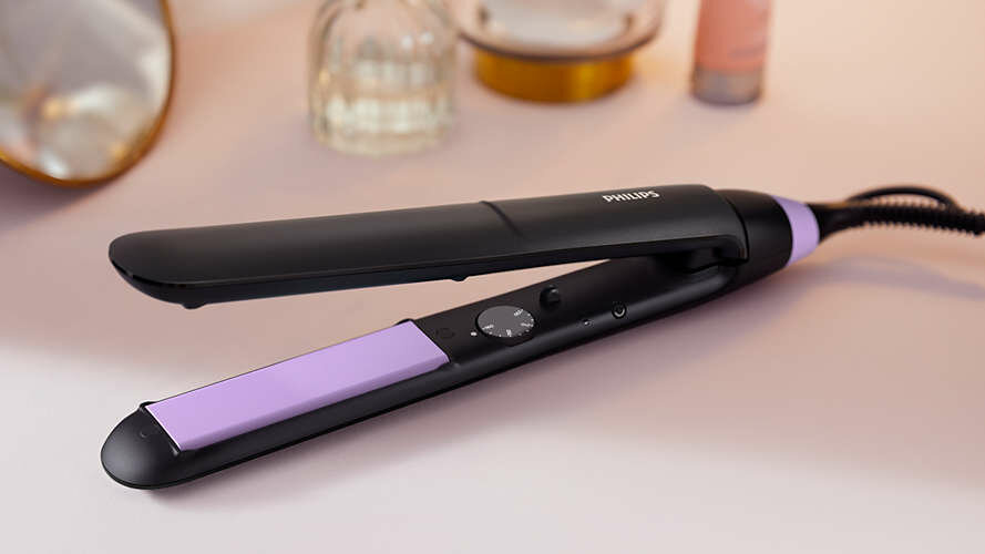 Czarna prostownica Philips z fioletową płytką leży na różowej powierzchni.