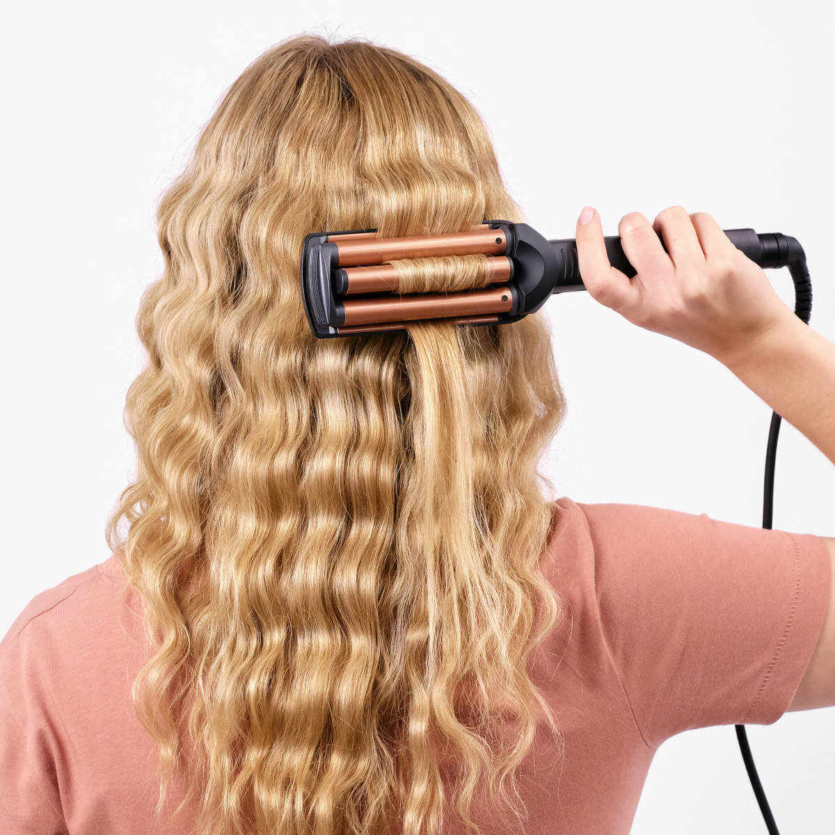Kobieta używająca falownicy do włosów, z pofalowanymi włosami i narzędziem w użyciu.