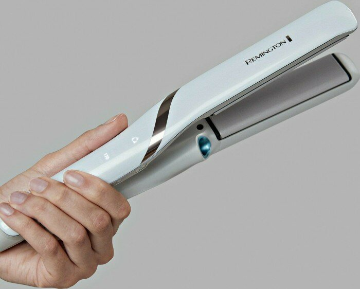 Dłoń osoby trzyma białą prostownicę Remington. Urządzenie jest otwarte i pokazuje płytki grzewcze.
