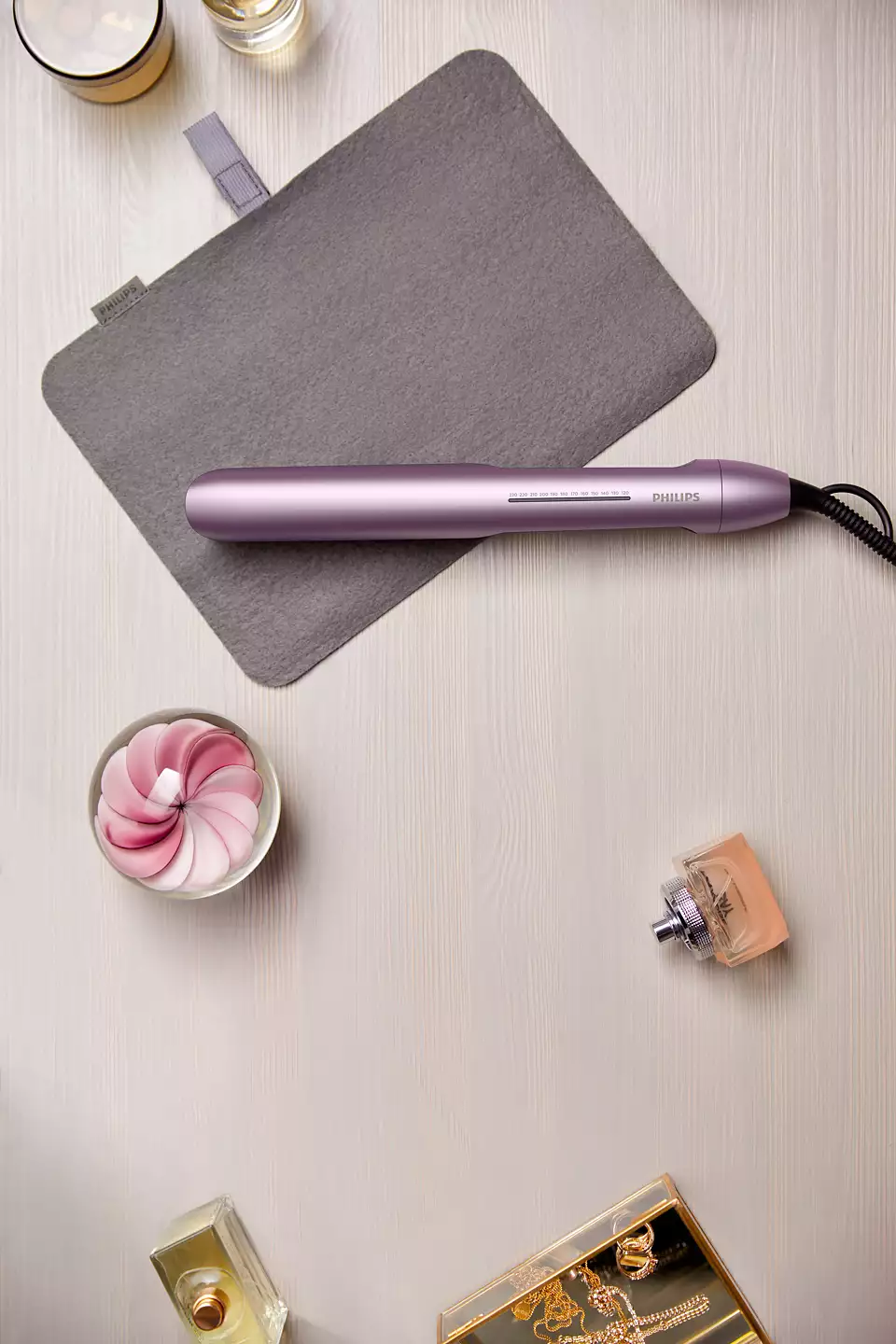 Prostownica, etui, perfumy i inne produkty kosmetyczne na drewnianej powierzchni.