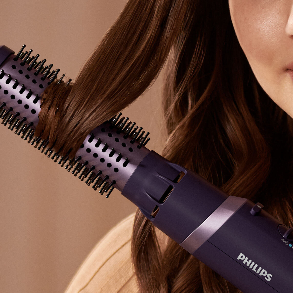 Lokówka do stylizacji brązowych włosów. Fioletowa i czarna lokówka w pobliżu twarzy kobiety.