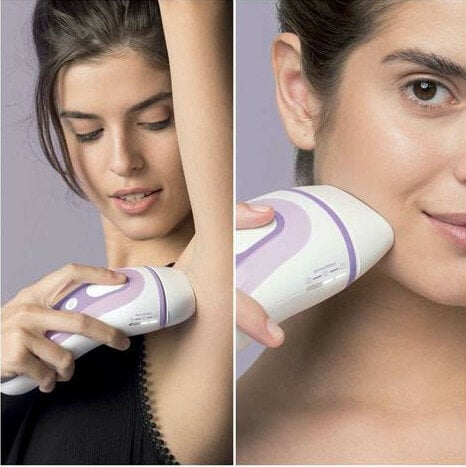 Kobieta używa urządzenia do usuwania włosów pod pachą i na twarzy. Urządzenie biało-fioletowe.