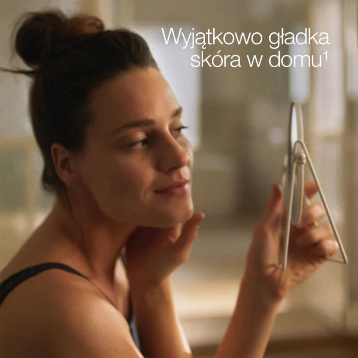 Kobieta przegląda się w lustrze, trzymając je. Tekst mówi: Wyjątkowo gładka skóra w domu.