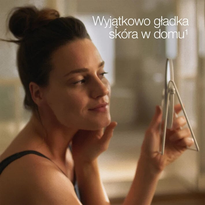 Kobieta patrzy na siebie w lustrze, dotykając twarzy. Tekst: Wyjątkowo gładka skóra w domu.