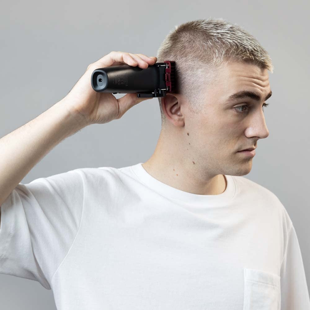 Mężczyzna używający czarnej maszynki do włosów na głowie, trzymając ją lewą ręką.