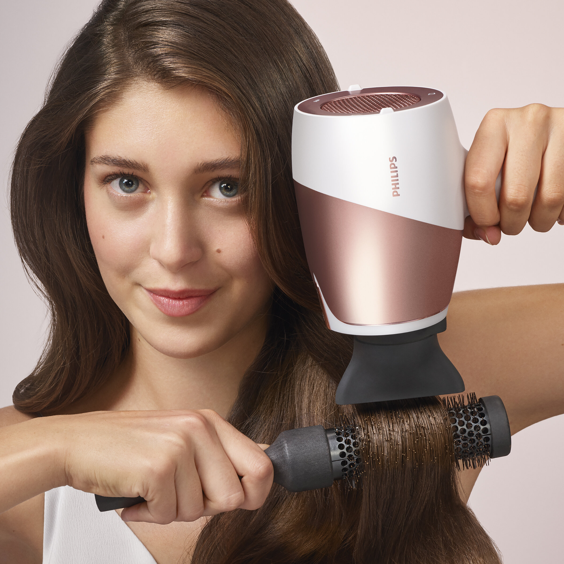 Kobieta z brązowymi włosami używająca różowo-białej suszarki do włosów.