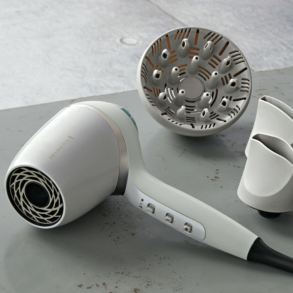Biała suszarka do włosów z nasadkami na szarej powierzchni. Suszarka ma przyciski i dyszę.