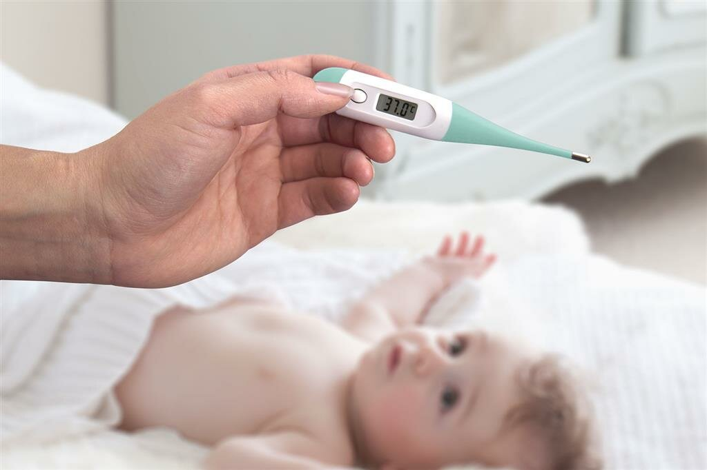 Dłoń trzymająca termometr z 37,0 stopniami nad dzieckiem.