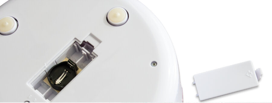 Zbliżenie na spód białego urządzenia z przegródką na baterie i drzwiczkami.