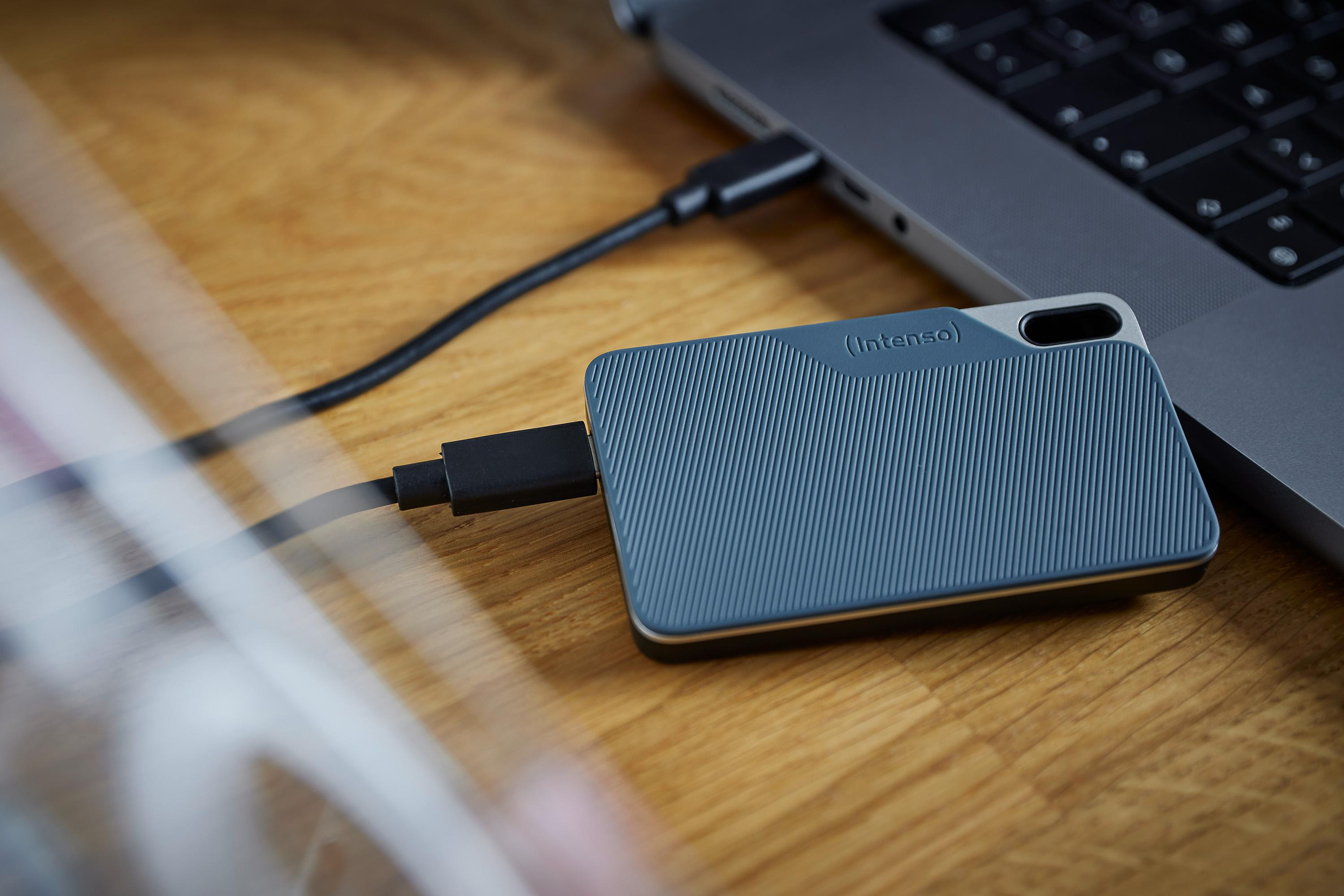 Externe Festplatte über USB-Kabel mit Laptop auf einem Holztisch verbunden.