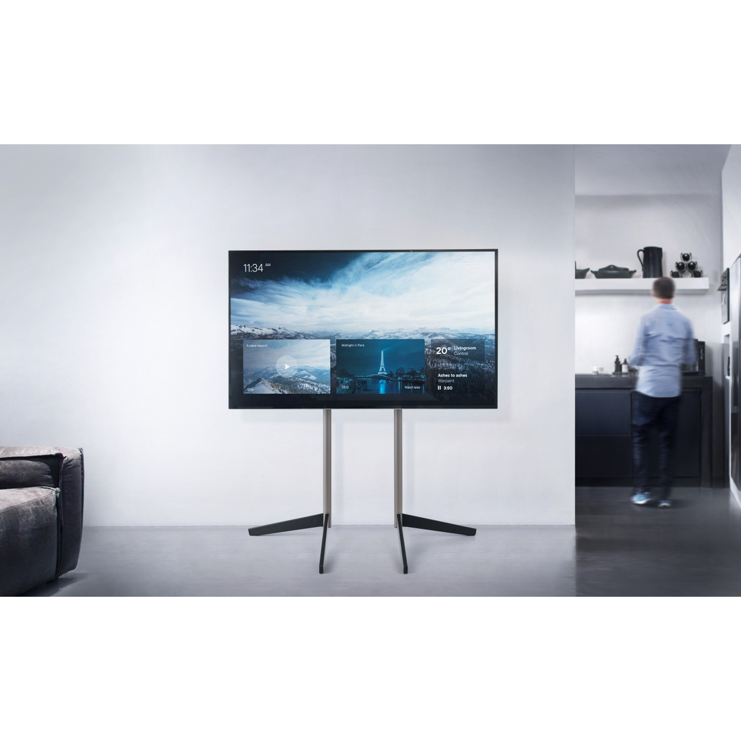 Moderne tv op standaard, met een scherm met een landschap. Man loopt op de achtergrond.