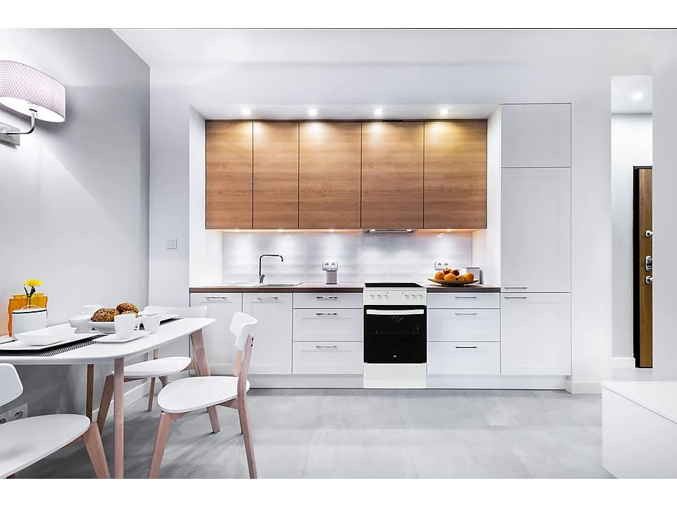 Moderne Küche mit weißen Schränken, Holzoberschränken und einem weißen Tisch mit Stühlen.
