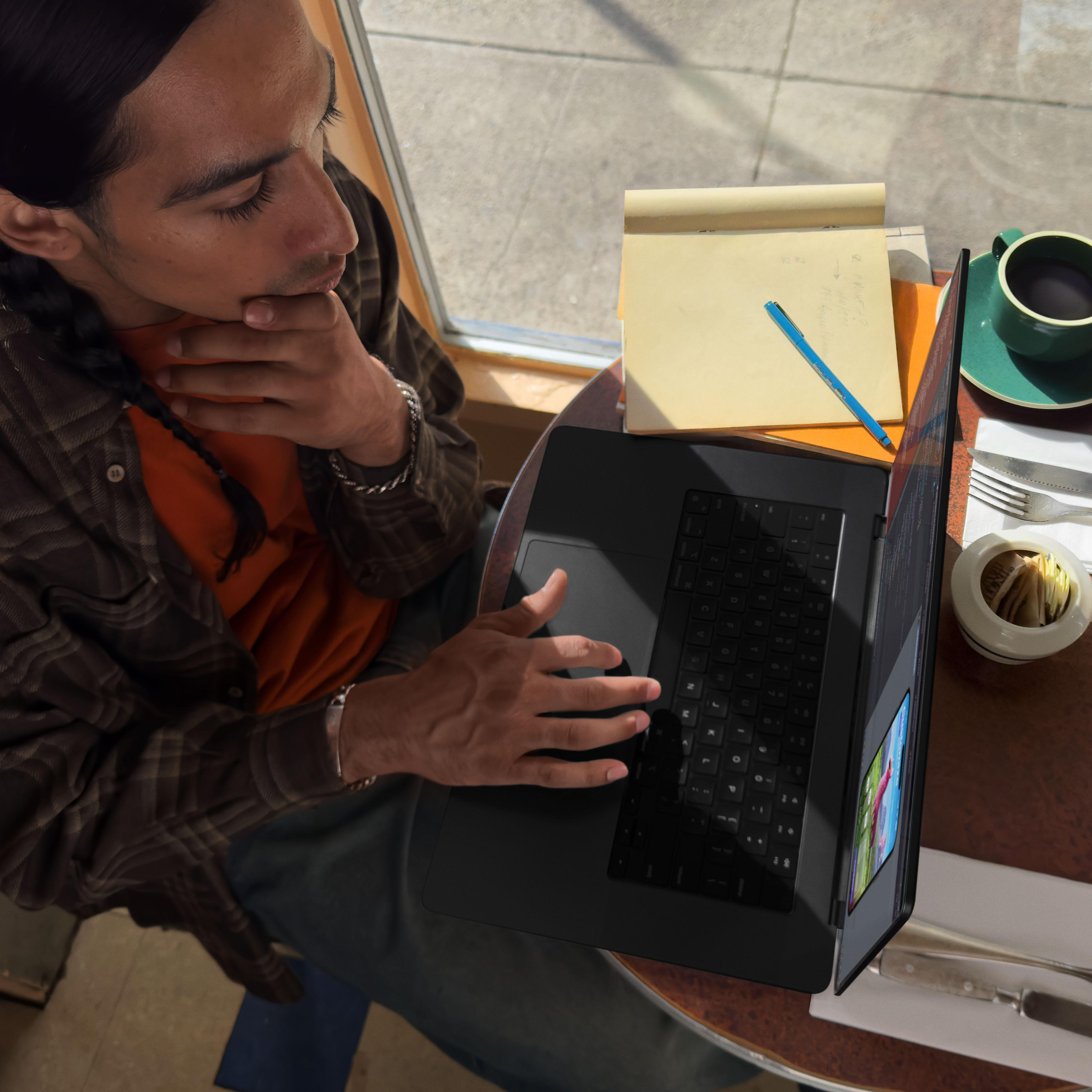 Draufsicht einer Person, die an einem Laptop an einem Tisch arbeitet, mit einer Kaffeetasse und einem Notizblock.