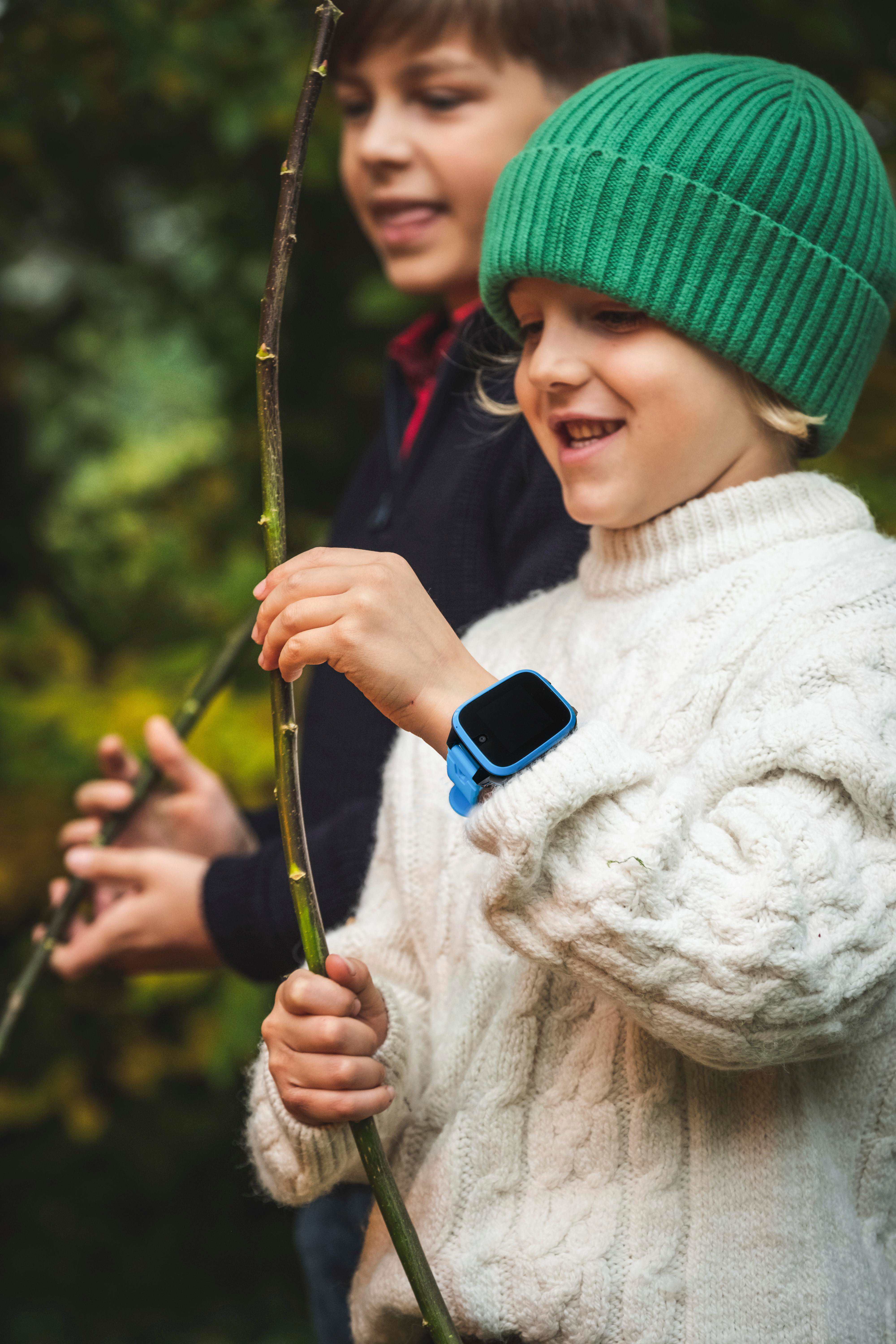Zwei Kinder spielen draußen. Eines trägt eine Smartwatch und hält einen Stock.