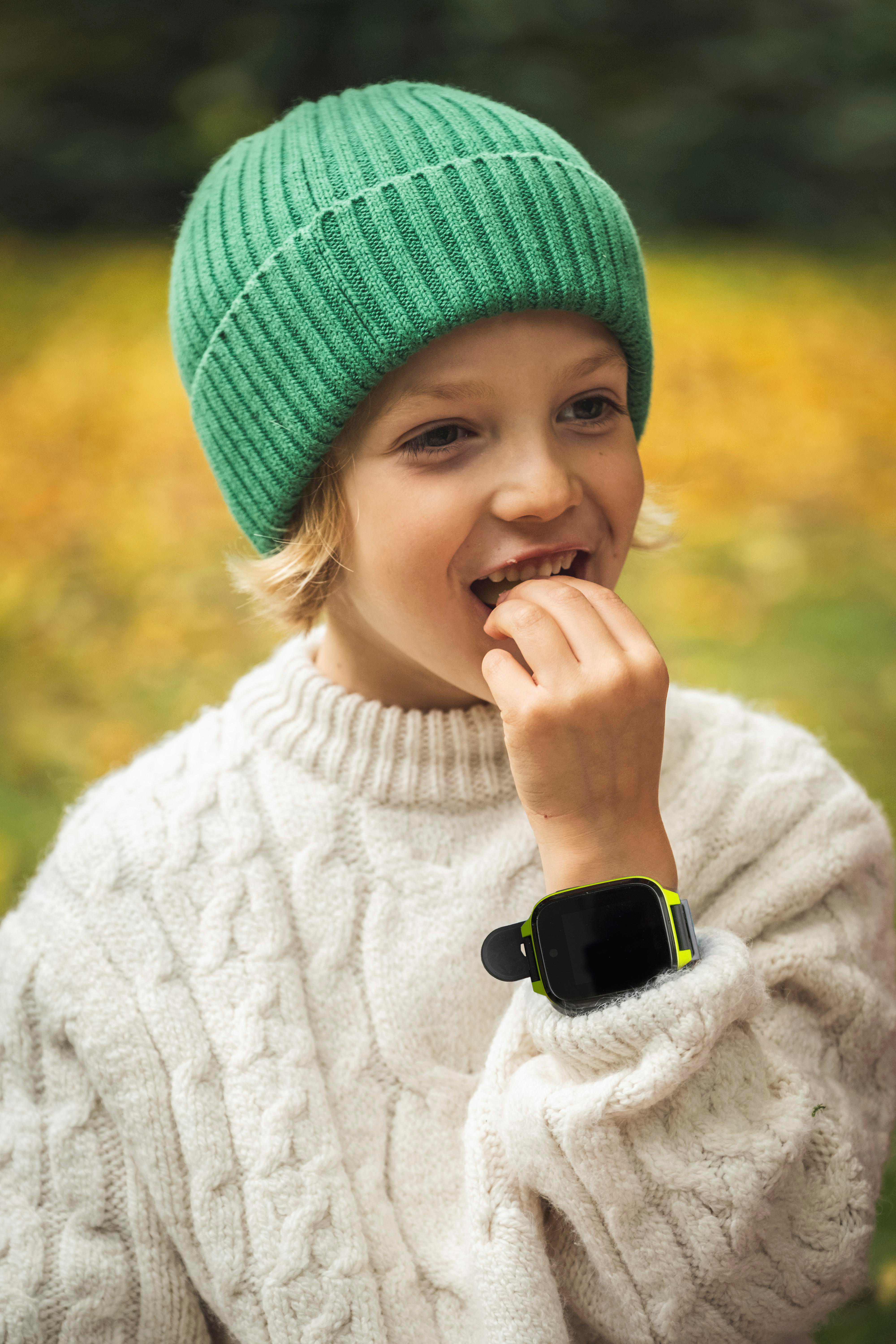 Ein junger Junge mit grüner Mütze und Smartwatch am Handgelenk lächelt.