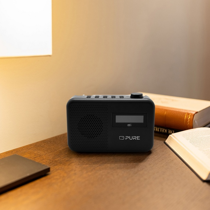 Une radio noire est posée sur une table en bois à côté de livres et d'une lampe.