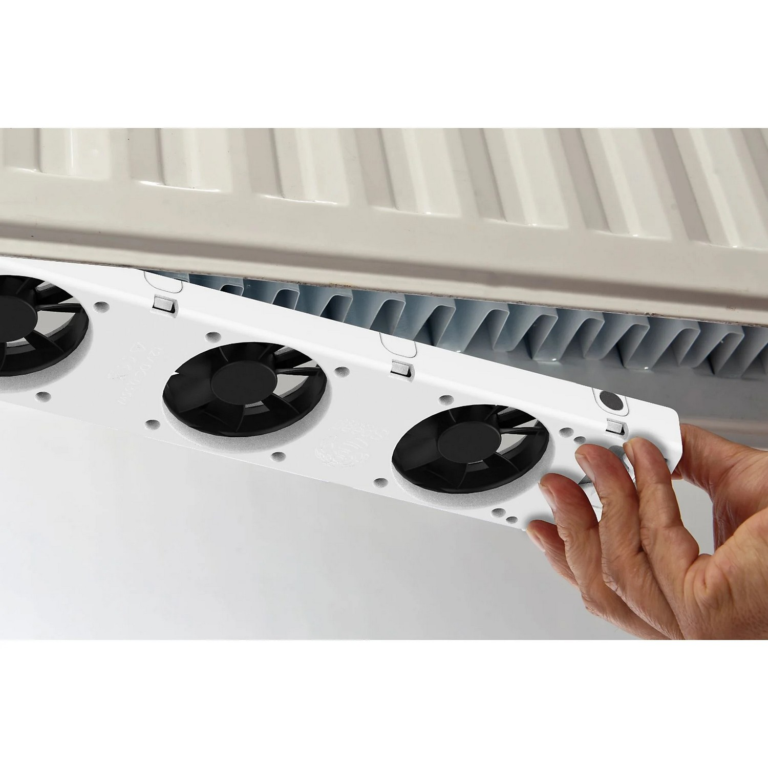A person is holding a white fan with black fans installed, placed on a radiator.