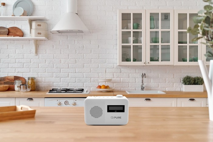 Une radio blanche avec un affichage numérique est posée sur une table en bois dans une cuisine.