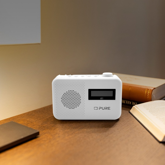 Radio blanche sur table en bois, à côté de livres. La radio a un écran et un haut-parleur.