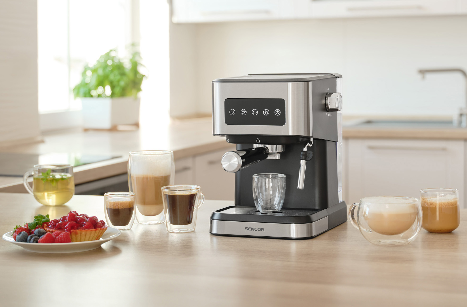 Espresszó gép kávéscsészékkel és péksüteményekkel egy faasztalon, konyhai háttérrel.