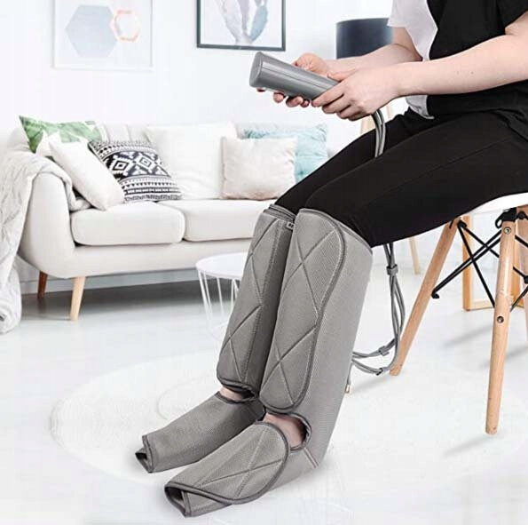 Osoba siedząca używa masażerów nóg, z pilotem w ręku, w pomieszczeniu.