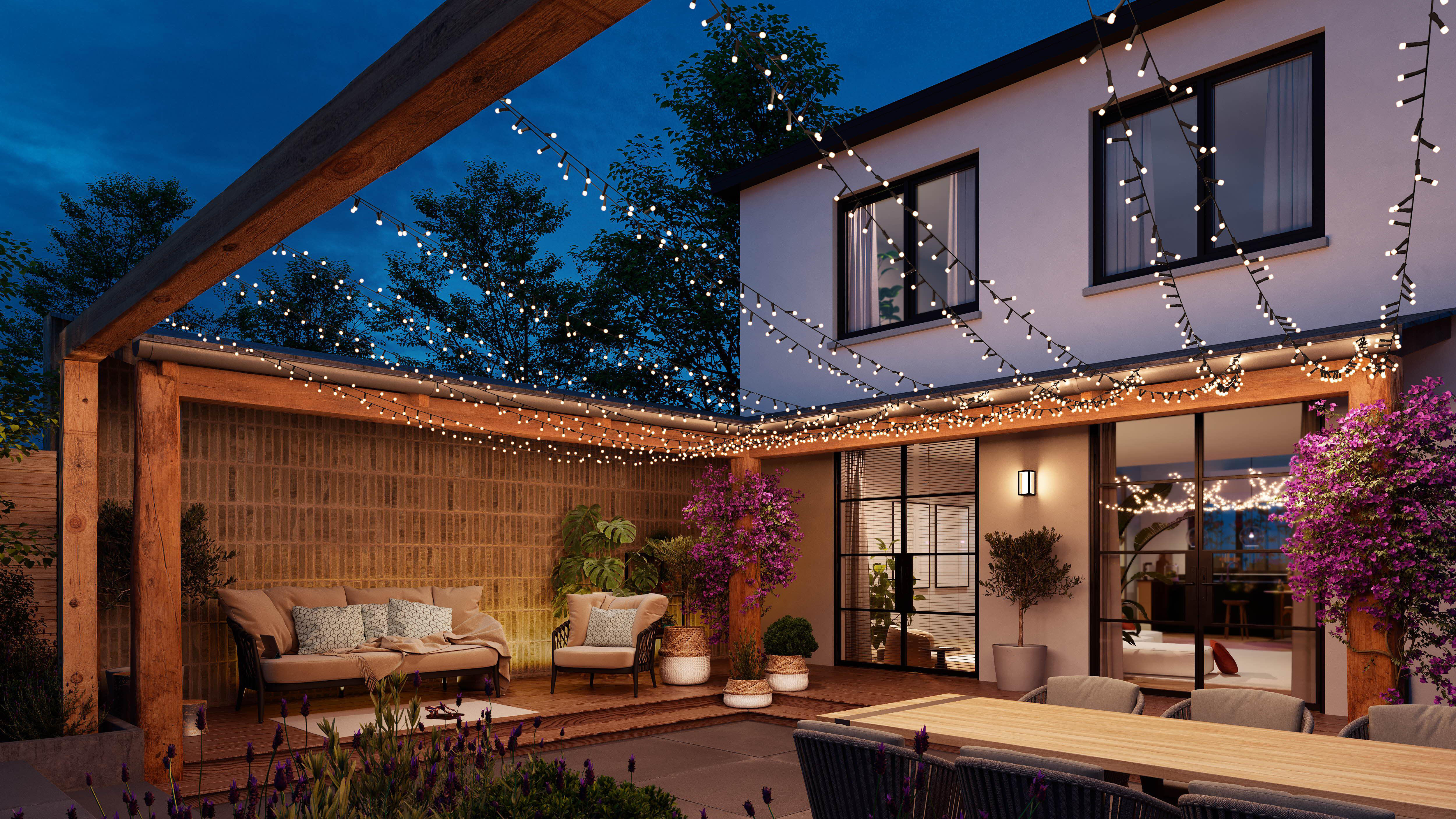 Hinterhofszene bei Nacht. Eine Terrasse mit Holzterrasse, Lichtern und Möbeln. Bäume im Hintergrund.