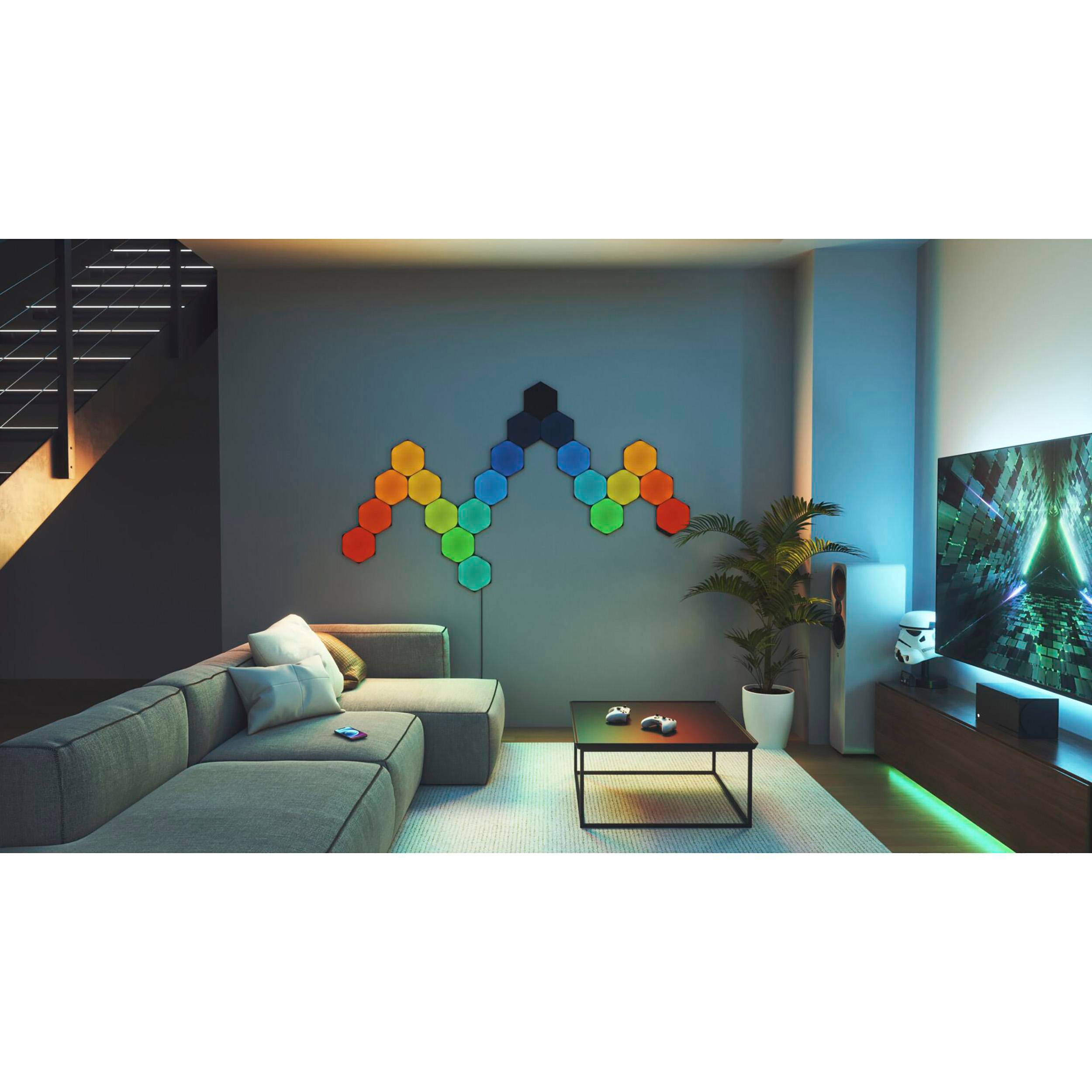 Ein Wohnzimmer mit einem grauen Ecksofa, einem Fernseher und einer Wand mit bunten sechseckigen Lichtern.