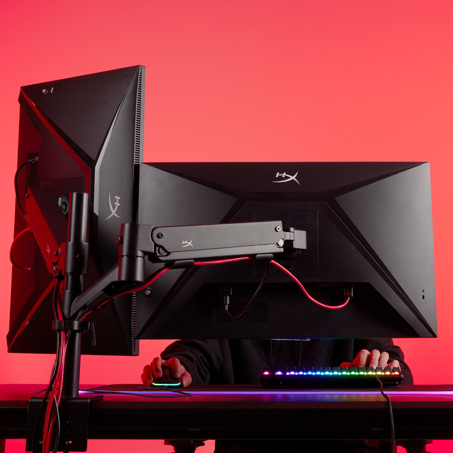 Gamer die een dual-monitor setup gebruikt met een toetsenbord en muis. Rode achtergrond.