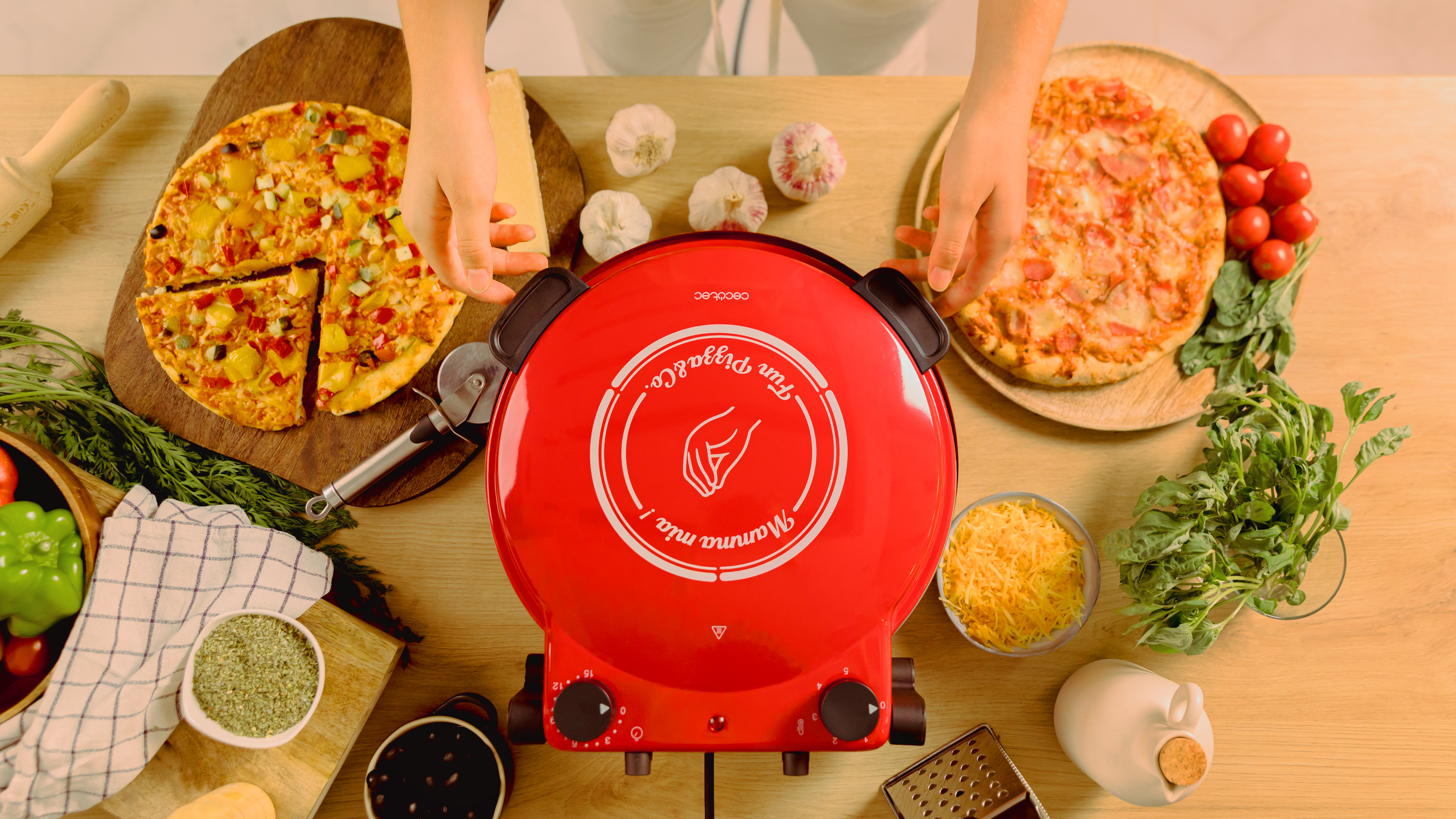 Toma cenital de una máquina para hacer pizza roja con pizzas, ingredientes y manos en acción.