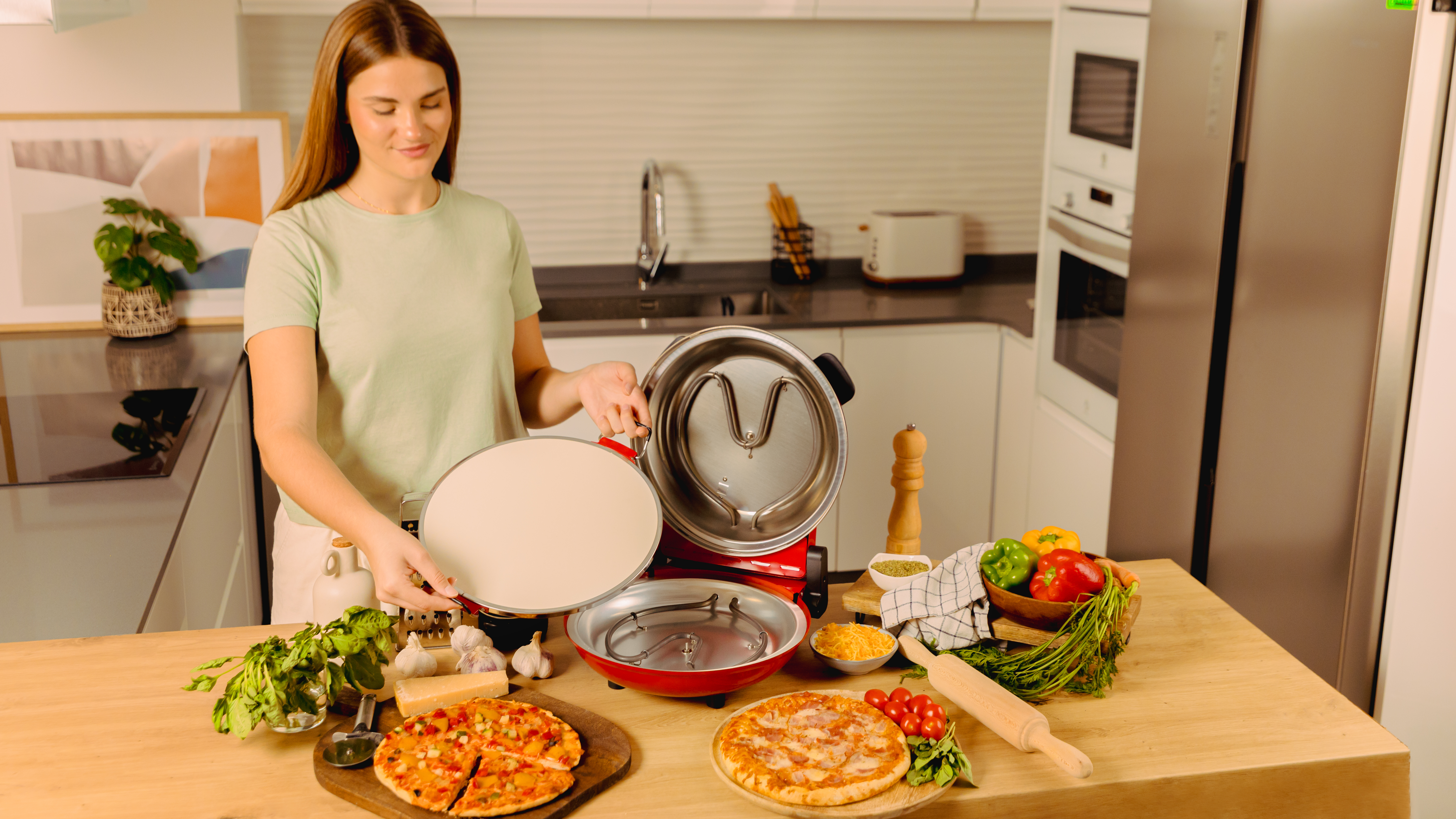Mujer sosteniendo una piedra para pizza cerca de un horno de pizza con ingredientes en una mesa.