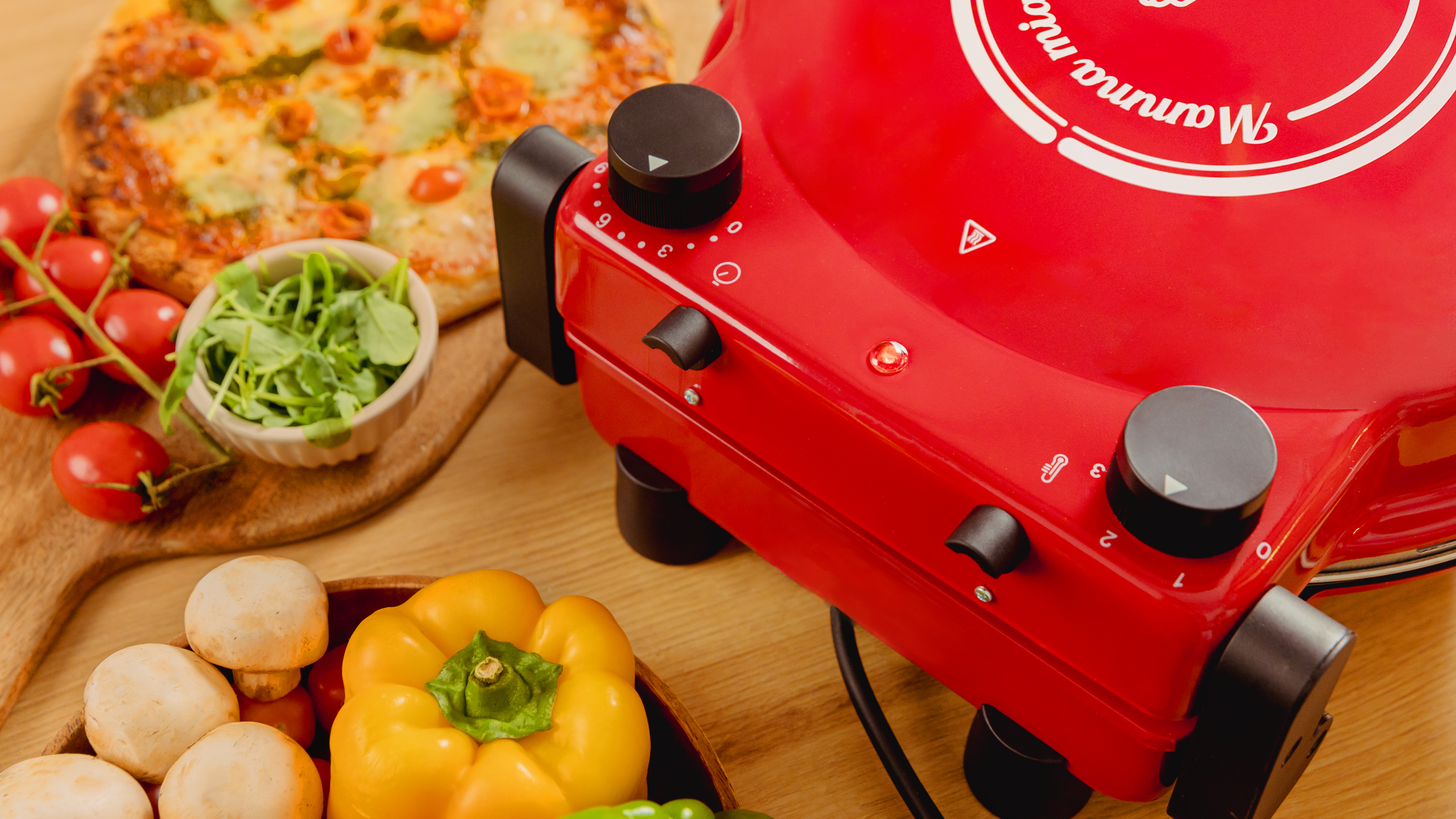 Horno de pizza rojo con pizza, verduras e ingredientes sobre una superficie de madera.