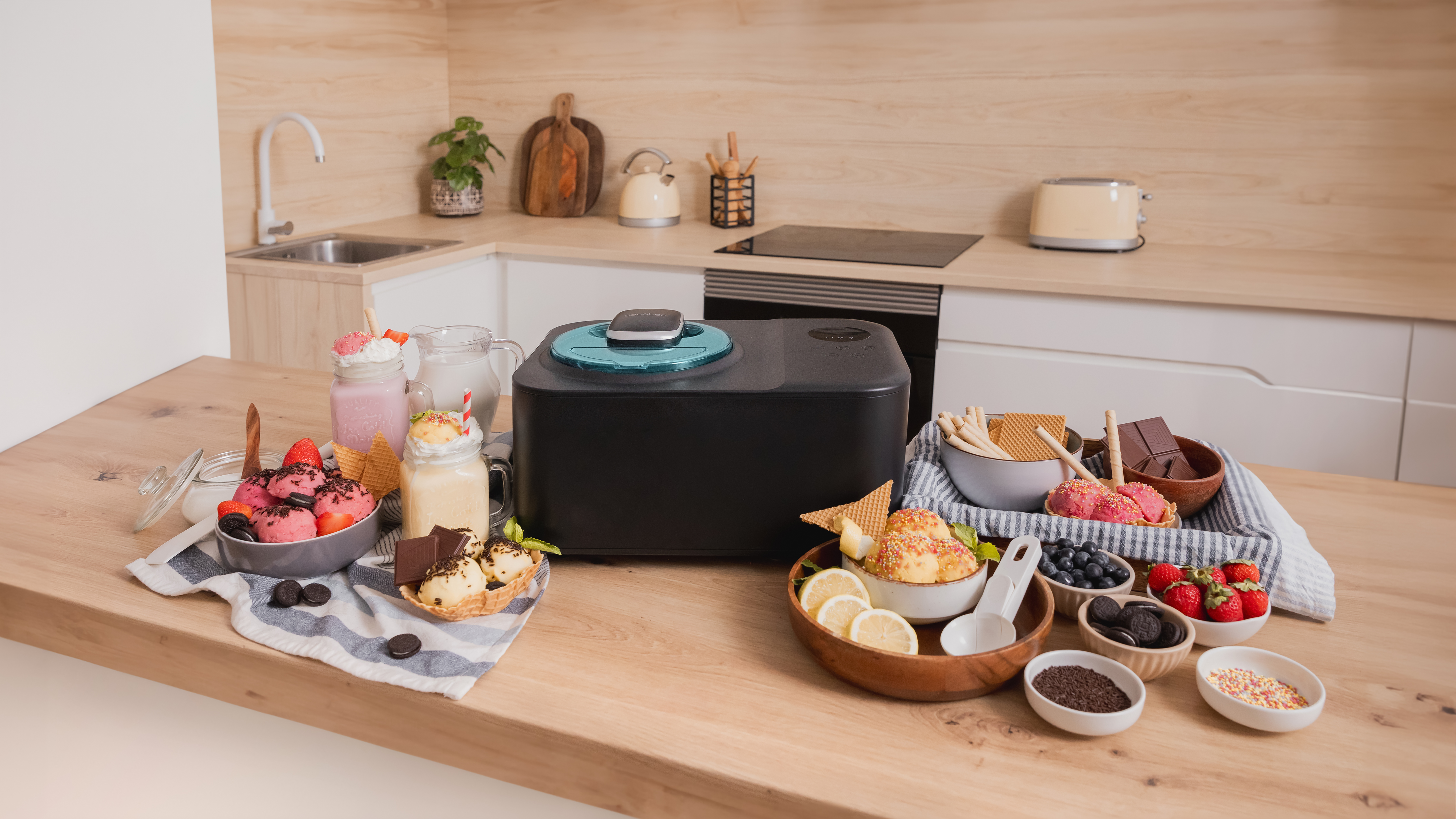 Escena de cocina con máquina de hacer helados y varios cuencos de helado y coberturas en una encimera de madera.