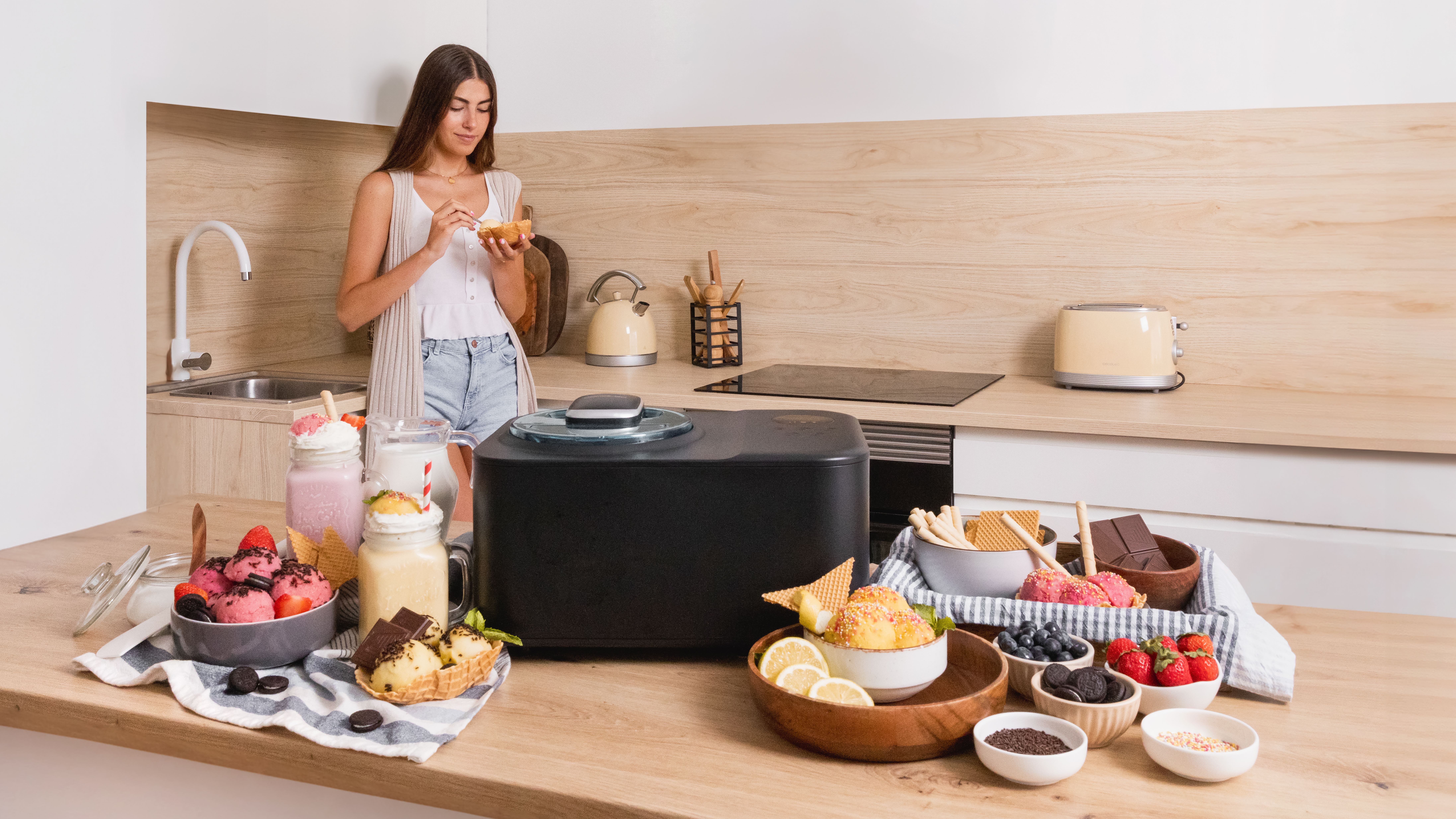 Una mujer en una cocina con helado y aderezos. Varias creaciones de helado en la mesa.