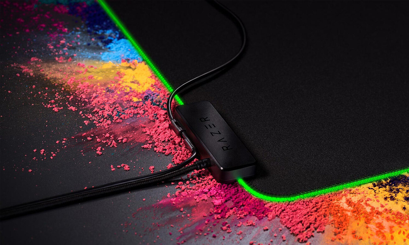 Czarna podkładka pod mysz z kolorowym pyłem wokół czarnego huba Razer z zielonym światłem.