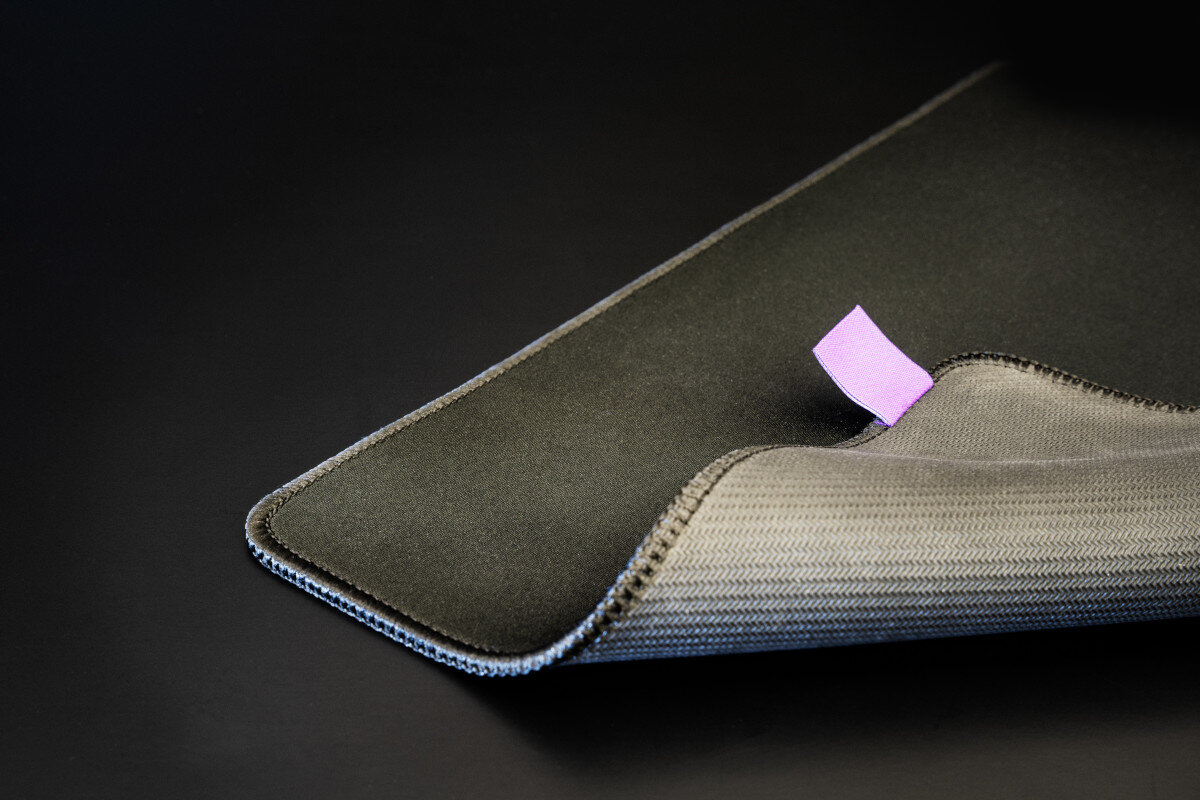 Zbliżenie czarnej podkładki pod mysz z wystającą fioletową etykietą. Tył jest szary.