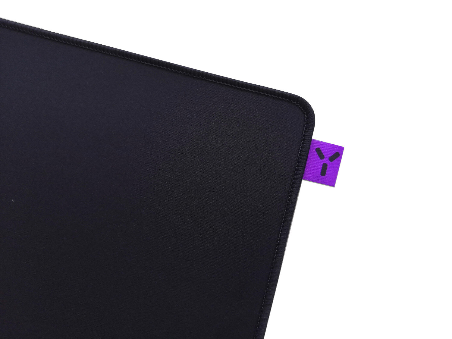 Zbliżenie czarnej podkładki pod mysz z fioletową metką i zszytą krawędzią na białym tle.