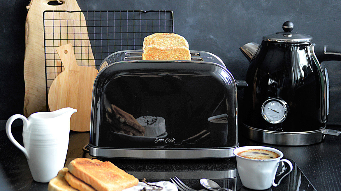 Czarny toster z chlebem, czajnik, filiżanka kawy i deski do serwowania.