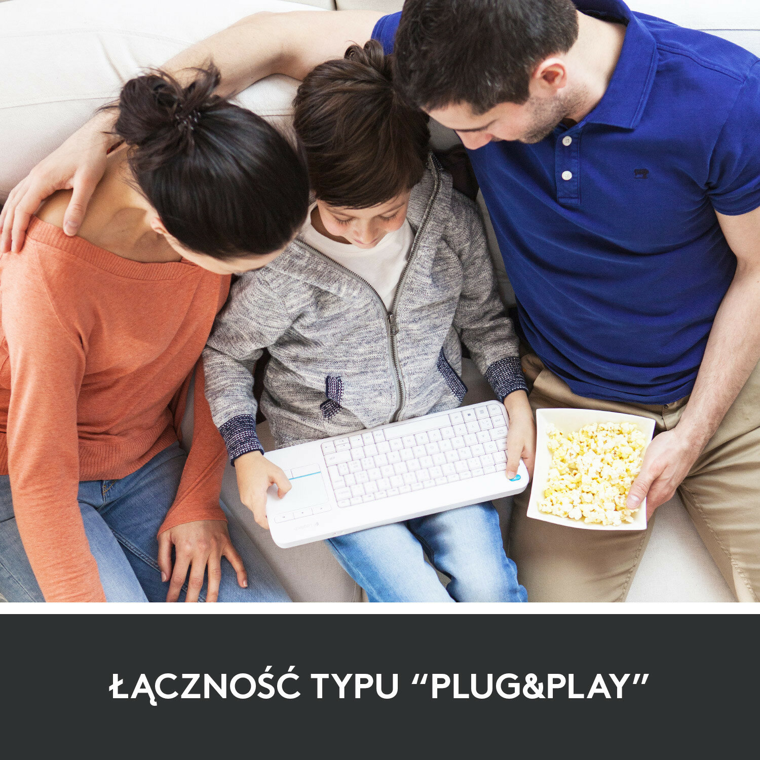 Rodzina patrzy na klawiaturę, trzymając popcorn. Tekst na dole brzmi 'PLUG&PLAY'.
