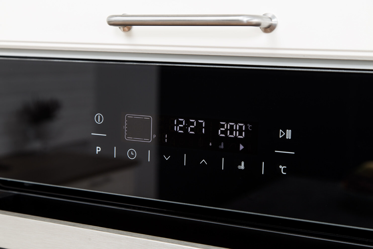 Panel sterowania piekarnika z wyświetlaczem cyfrowym, pokazujący godzinę i temperaturę, z białą szafką powyżej.