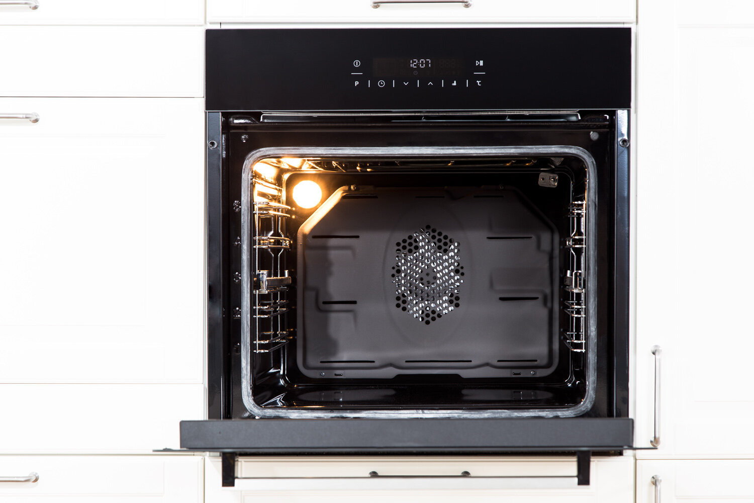 Otwarty piekarnik w białej kuchni. Widoczne wnętrze, ze światłem i wentylatorem.