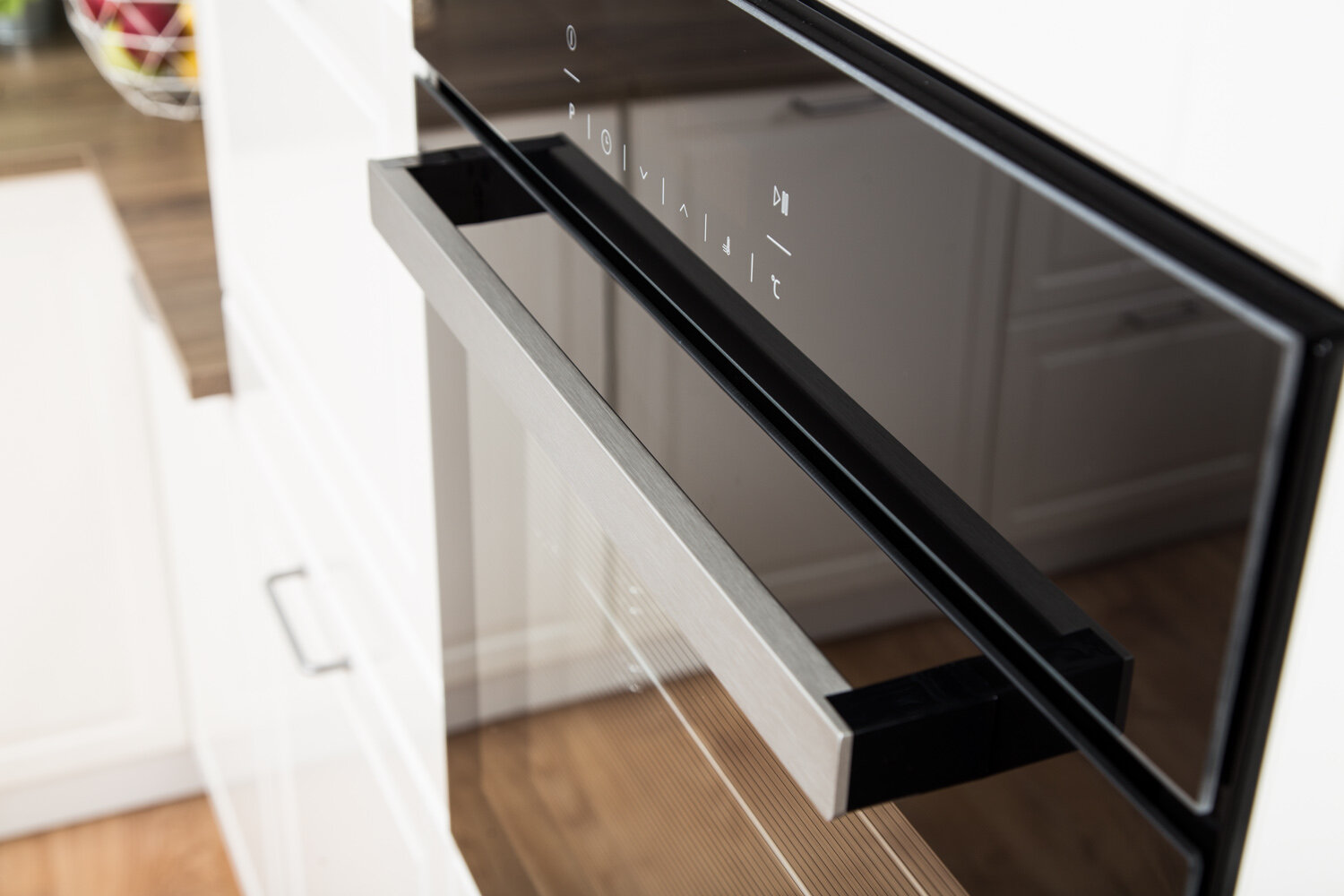 Zbliżenie czarnego piekarnika ze srebrnym uchwytem, w białej kuchni.