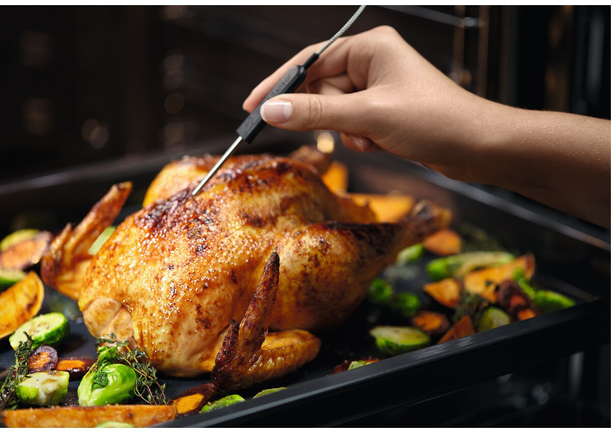 Dłoń wkładająca termometr do pieczonego kurczaka w piekarniku.