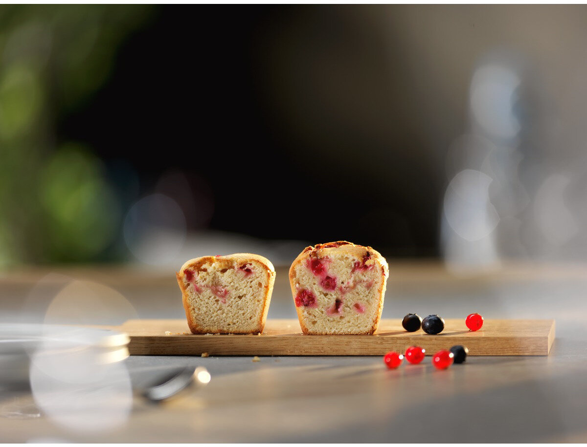 Dwie połówki muffina z czerwonymi jagodami na drewnie. Jagody rozrzucone na stole. Tło jest rozmyte.